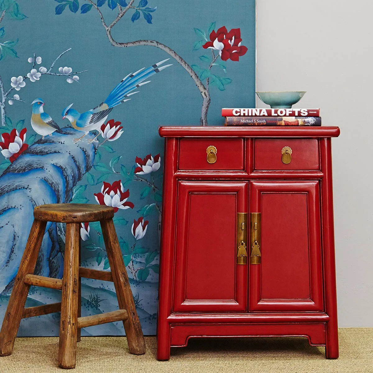 A wooden stool and red cabinet set against lovely blue wallpaper