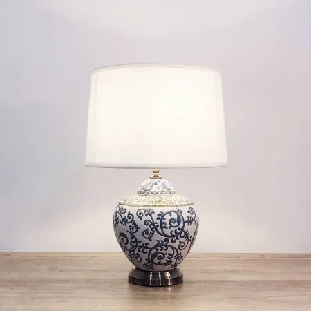 A round ceramic table lamp with a white base with blue and green floral lines and a metallic base