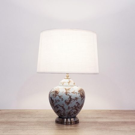 A round ceramic table lamp with a light blue base with light brown/beige floral designs and a metallic base