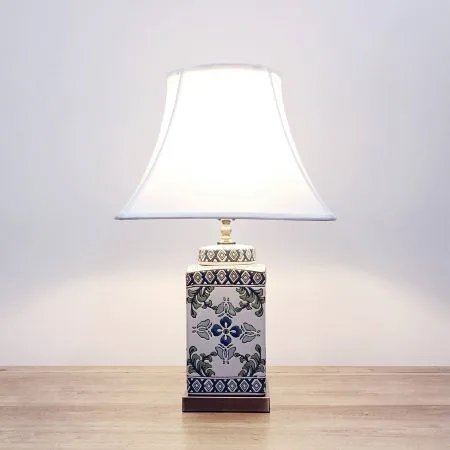A square ceramic table lamp with a white base with green & blue floral designs and a metallic base