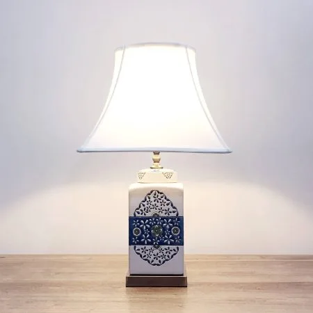 A square ceramic table lamp with a white base with green & blue floral motifs and a metallic base