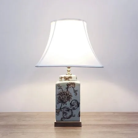 A square ceramic table lamp with a light blue base with light brown/beige floral designs and a metallic base