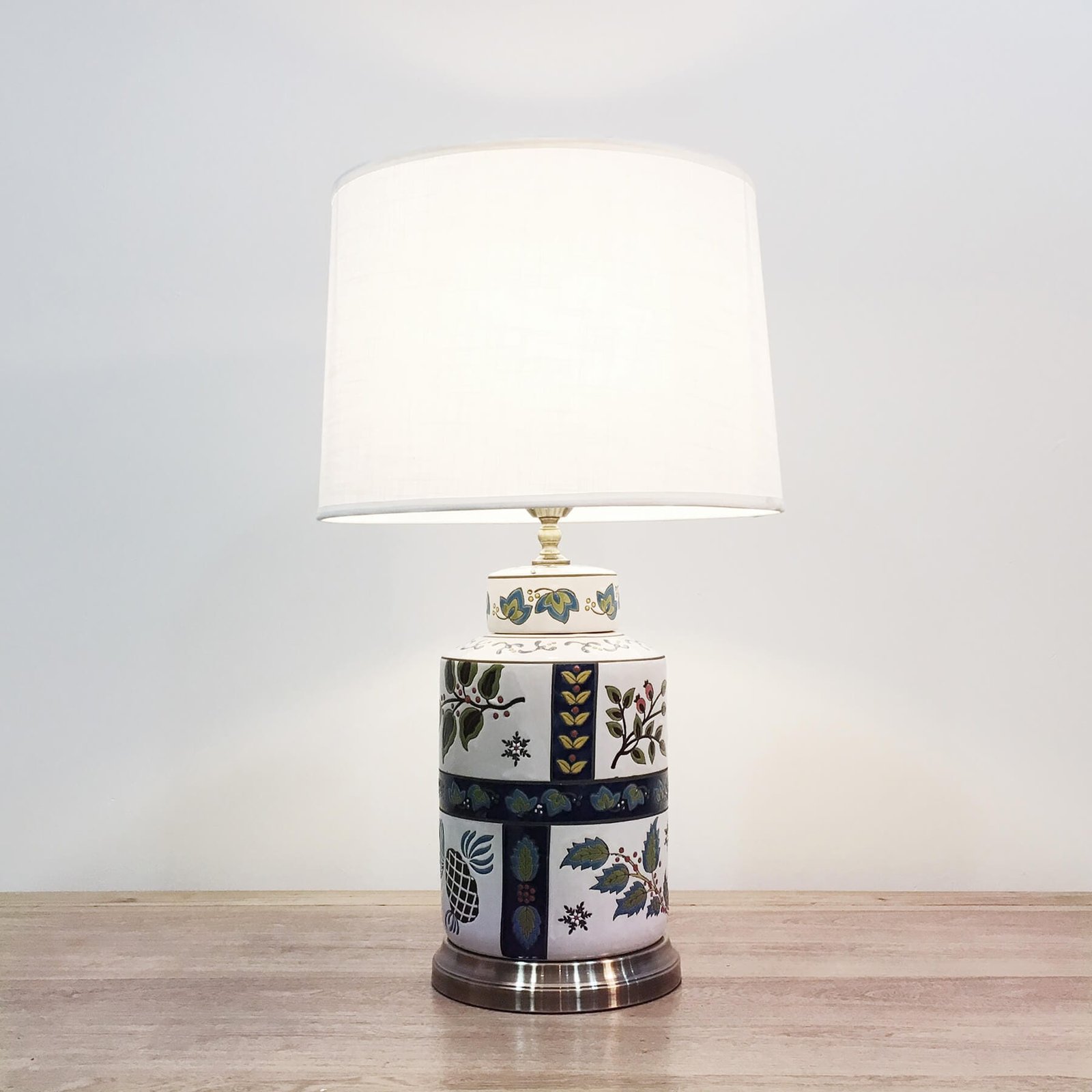 A cylindrical ceramic table lamp with white background and simple floral designs and a metal base