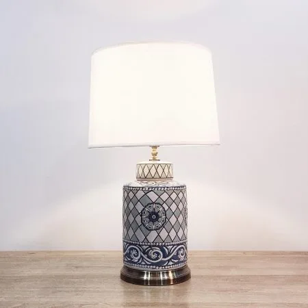 A cylindrical ceramic table lamp with blue, aqua & white patterns and a metal base
