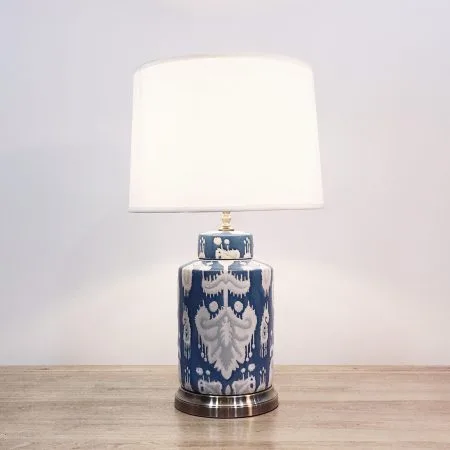 A round ceramic table lamp with a blue base and “ikat” design and a metallic base.