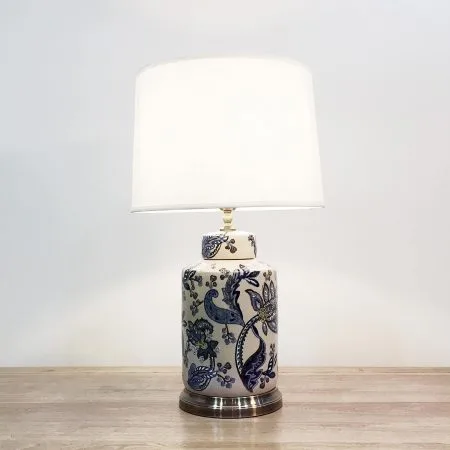 A cylindrical ceramic table lamp with blue & white paisley print against a cream background and a metal base