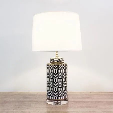 A cylindrical ceramic table lamp with black & white geometric patterns and an acrylic base.