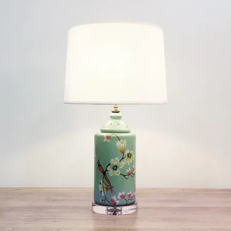 A round ceramic table lamp with a light turquoise green base with birds & flowers motifs and an acrylic base