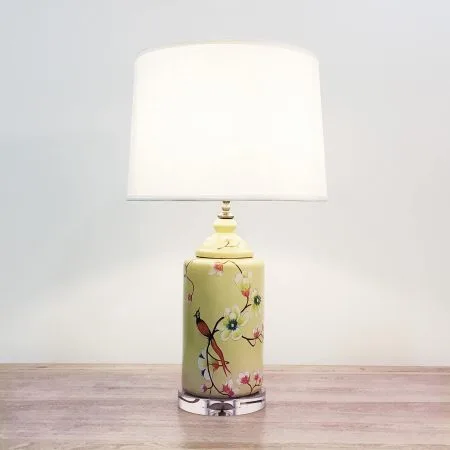 A round ceramic table lamp with a yellow base with birds & flowers motifs and an acrylic base