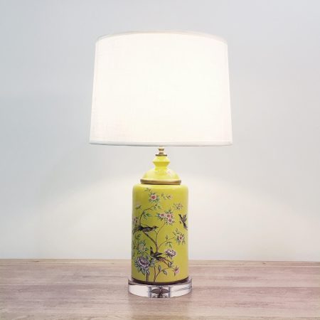 A round ceramic table lamp with a vibrant yellow base with birds & flowers motifs and an acrylic base