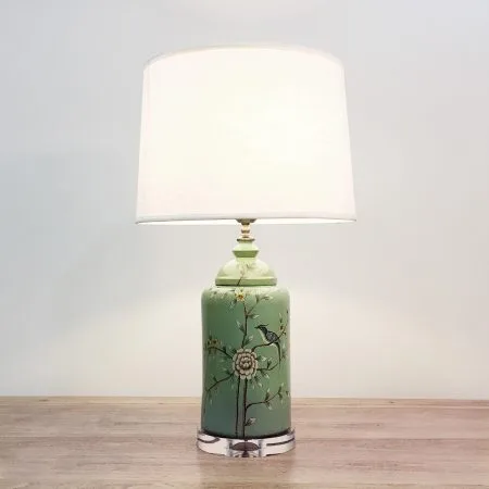 A round ceramic table lamp with a light green base with birds & flowers motifs and an acrylic base