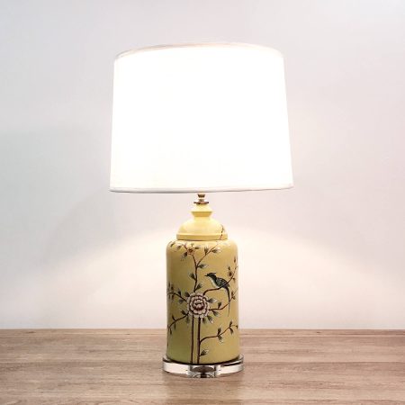 A round ceramic table lamp with a yellow base with birds & flowers motifs and an acrylic base