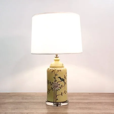 A round ceramic table lamp with a yellow base with birds & flowers motifs and an acrylic base