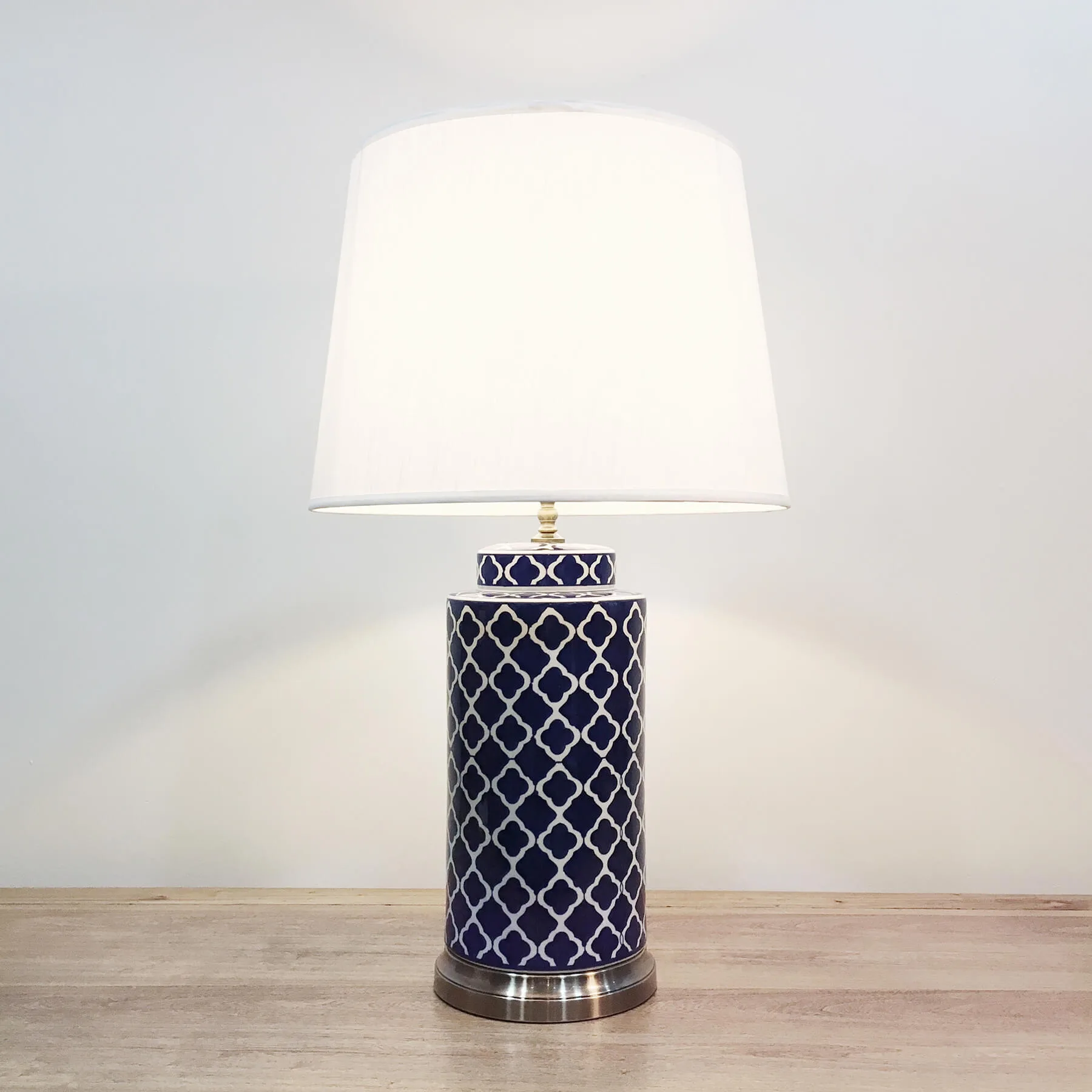 A tall cylindrical ceramic table lamp with white “cherry-blossom” patterns against a dark royal blue background and a metal base