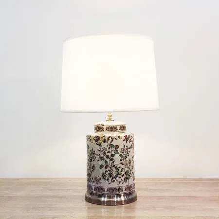 A cylindrical ceramic table lamp with colourful floral patterns against a crackled beige background and a metal base