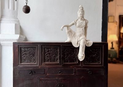 A ceramic white Guan Yin sitting on a Chinese antique small dark carved cabinet