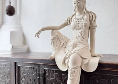 A ceramic white Guan Yin sitting on a Chinese antique small dark carved cabinet