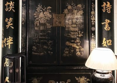 Chinese antique black lacquered and painted large Shanxi cabinet, flanked by a tall pair of calligraphy couplets