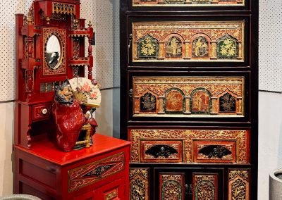 two carved pieces from Fujian. One is a red washbasin cabinet with carvings on top. The cabinet on the right is black with colourful carvings of slim swing doors