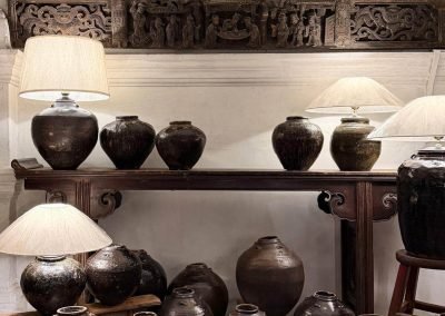 A long antique elmwood console table with upward-curving everted ends, a single-plank tabletop with beaded edge, cloud-shaped spandrels connecting the legs to the top, and an openwork cloud carving between the legs. Surrounded by a collection of vintage glazed ceramic pots of various sizes.
